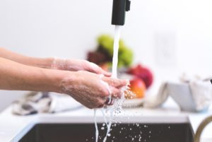 A person washing their hands with food ingredients in the background