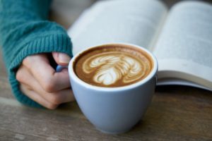 A person holding a mug of coffee while reading a book
