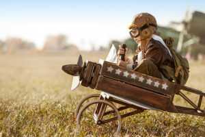 A kid riding a wooden plane replica with aviation gear
