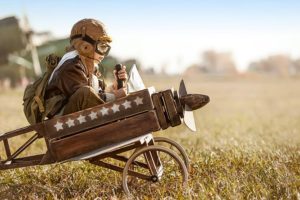 A kid riding a wooden plane replica with aviation gear