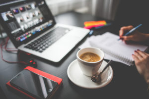 A person writing notes with a laptop and coffee