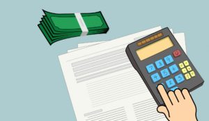 A person using a calculator on top of papers and beside paper money