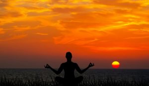 A person meditating at sunset