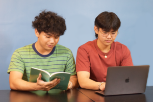 Two people sitting, one reading and one using their laptop